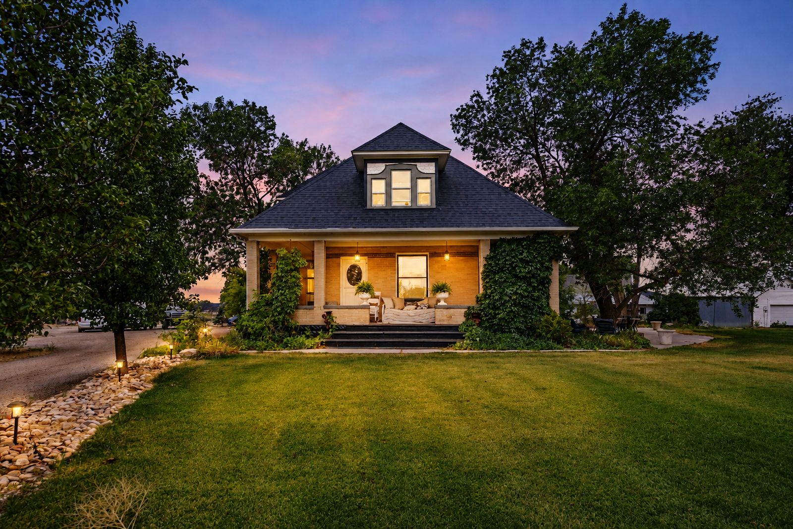The historic farmhouse at dusk, windows and porch lit