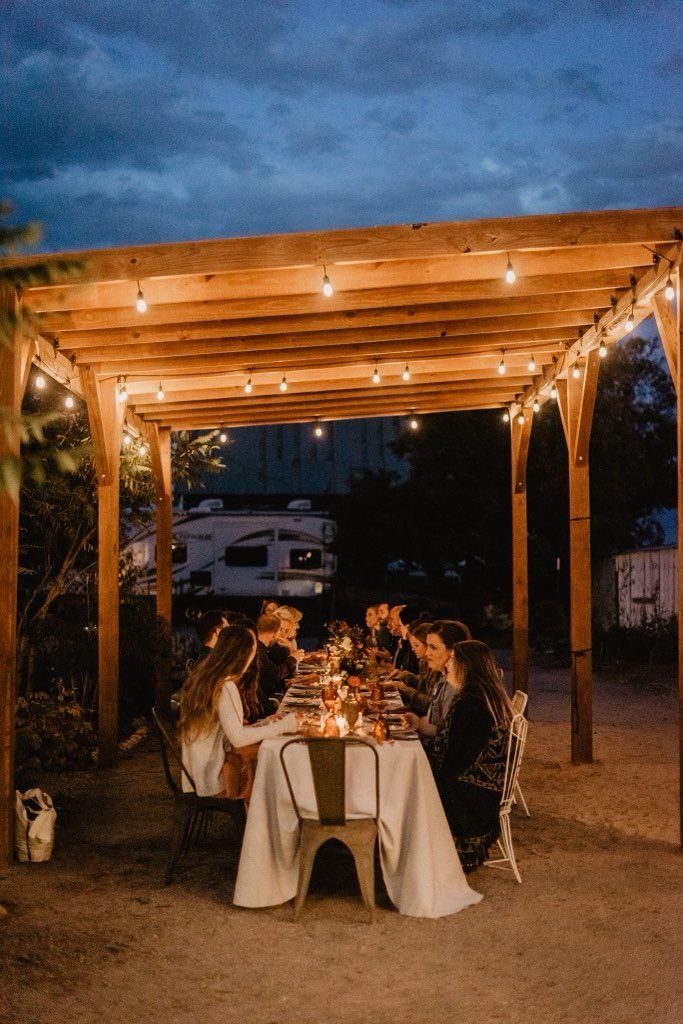 A candlelit farm dinner under the pavilion at night, string lights overhead and a long table of guests