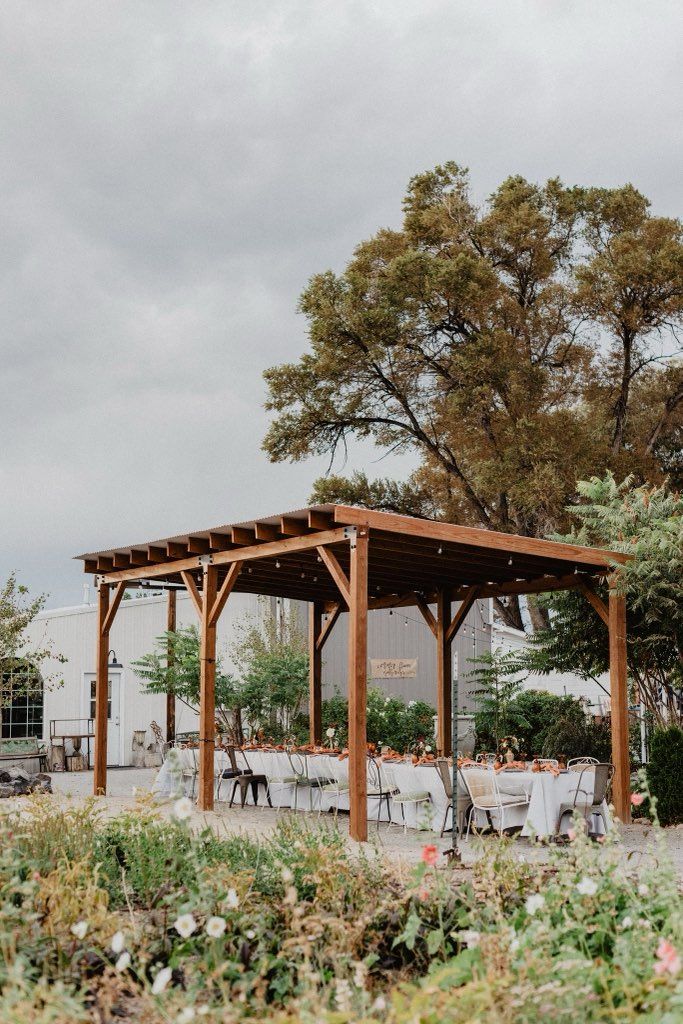The pavilion set for a wedding reception, tables dressed in white, flower beds in the foreground